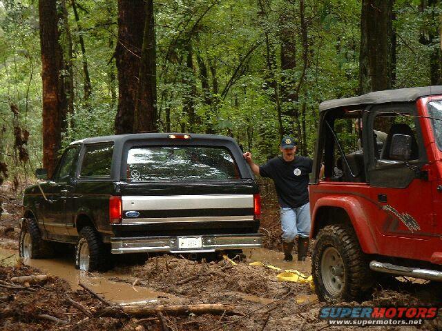 1995 Ford Bronco and red Jeep Wrangler stuck in muddy woods