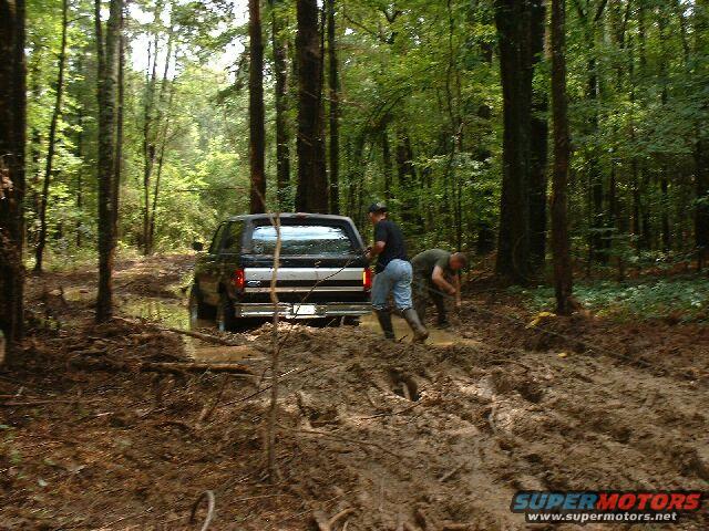 1995 Ford Bronco rear view stuck in mud with two people attempting recovery