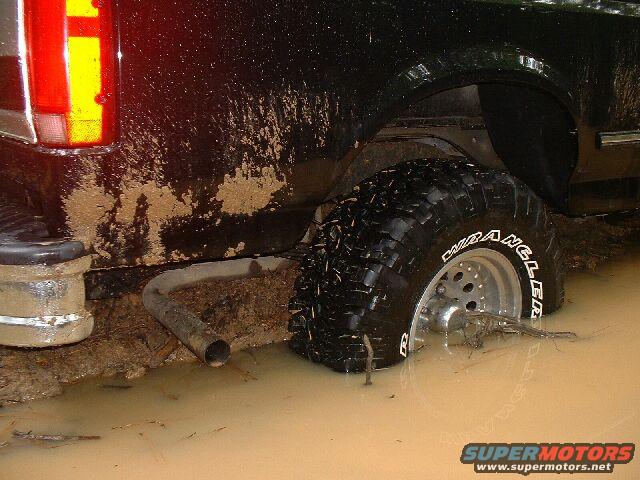 Rear tire of a black truck stuck deep in muddy water, exhaust pipe visible