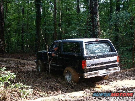 Black 1995 Ford Bronco driving through mud in a forest