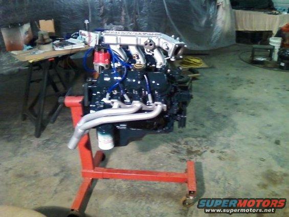 Engine on red stand, V6 configuration with chrome exhaust manifolds