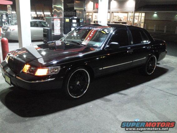 Black 2000 Mercury Grand Marquis parked at gas station, custom rims