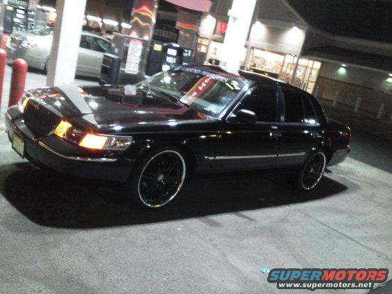 Black 2000 Mercury Grand Marquis with custom rims parked at a gas station