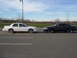 2000 Mercury Grand Marquis - A white and a black sedan are parked facing each other in a lot under a cloudy sky.