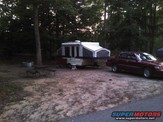 Maroon sedan parked next to a pop-up camper at a campsite