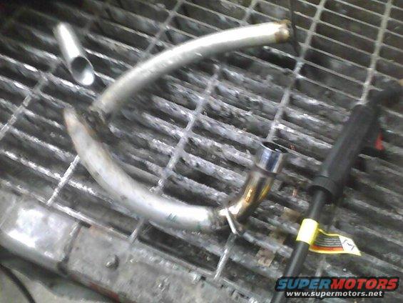 Curved metal exhaust pipe section on a metal grate, with a welding tool nearby
