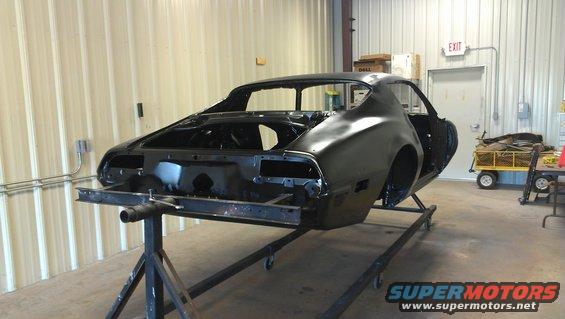 Black 1970s coupe car body on a metal stand, viewed from the rear three-quarter angle in a workshop
