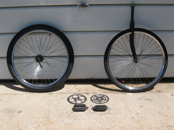 Two bicycle wheels, two chainrings, and two pedals laid out on concrete