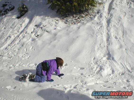 Child in purple jacket and blue snow pants kneeling in snow