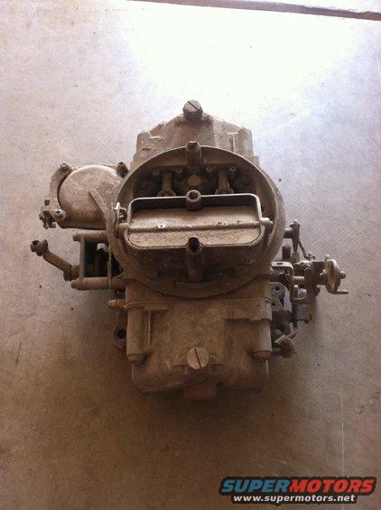 Dusty carburetor with visible linkages and screws, resting on a concrete surface