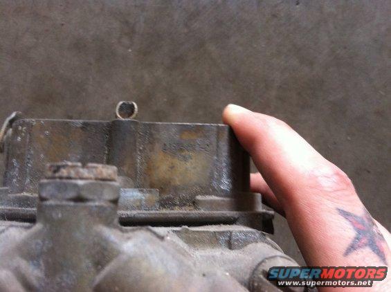 Close-up of a carburetor with a hand holding the top. Some numbers are visible on the side