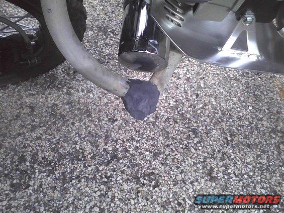 Close-up of a motorcycle's exhaust pipe with some dark putty applied where it connects