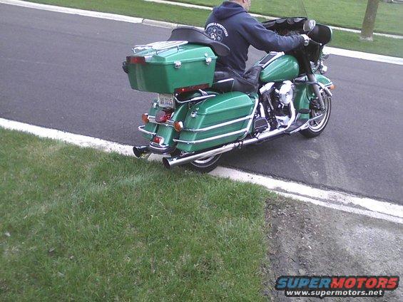 Green motorcycle with rider, rear view, chrome exhaust, luggage rack, and saddlebags