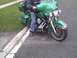 2003 Ford Crown Victoria - A green motorcycle with saddlebags is parked on the side of the road, with a person seated on it.