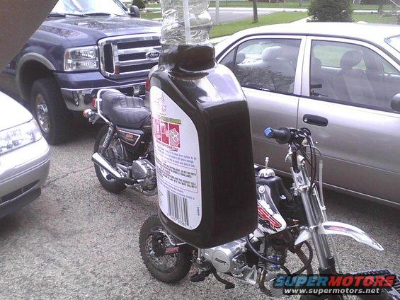 Motor oil bottle mounted on a dirt bike, with a classic motorcycle and Ford truck in the background