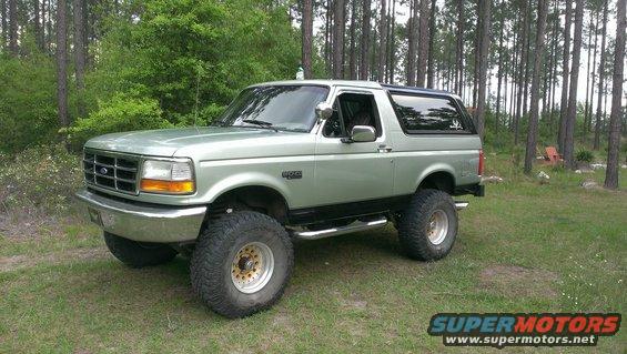 Lifted 1995 Ford Bronco parked in a grassy area with trees in the background