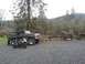 1979 Ford Bronco - A black Ford Bronco and a motorcycle sit in a gravel lot with trees and hills in the background.