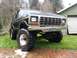 1979 Ford Bronco - This modified Ford Bronco sits high on large tires in a grassy yard next to a building.