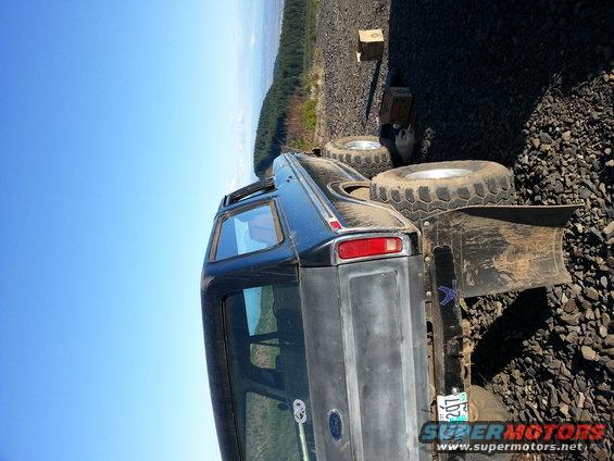 Black Ford Bronco with large tires parked on a rocky surface. Has a plow attachment on the rear