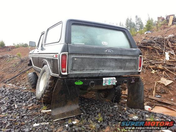 Black 1978 Ford Bronco with large tires and mud flaps, parked on rocky terrain
