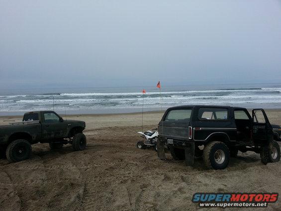 Black 1979 Ford Bronco with open door and quad bike on beach