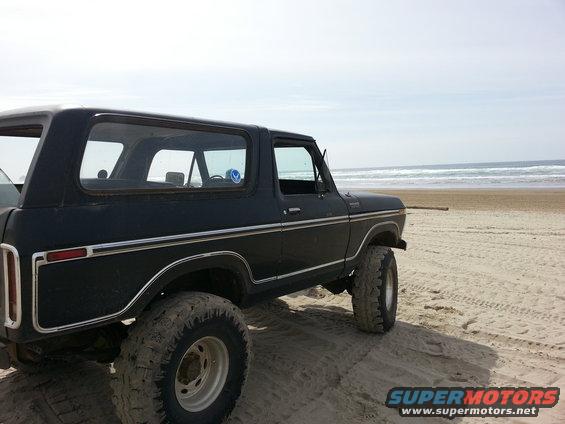 Black SUV parked on a sandy beach with the ocean in the background. The vehicle has large tires and chrome trim