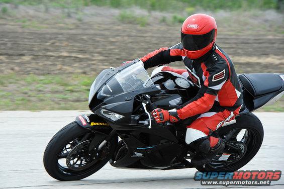 Motorcyclist in red and black gear on a black sportbike, wearing a red helmet