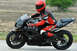 2001 Kawasaki KZ1000-A1 - A motorcyclist wearing a red helmet and racing suit rides a black sportbike on a paved road.