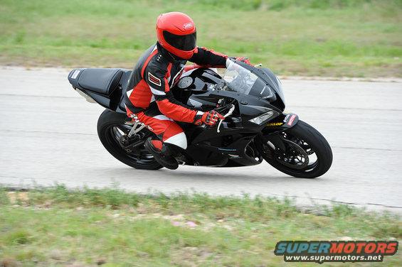 Rider in red and black gear on a black sportbike leans into a turn on a paved track