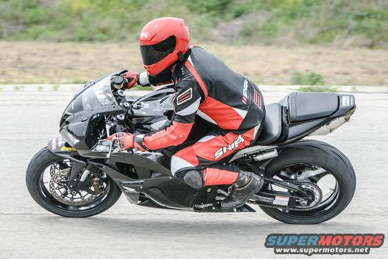 Black sport motorcycle with a rider in red and black gear, seen from the side