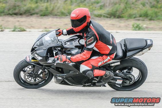 Side view of a black motorcycle with a rider in red and black gear, Supermotors logo visible