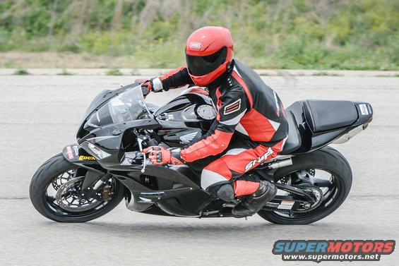 Motorcyclist wearing red and black leathers and a red helmet rides a black sportbike