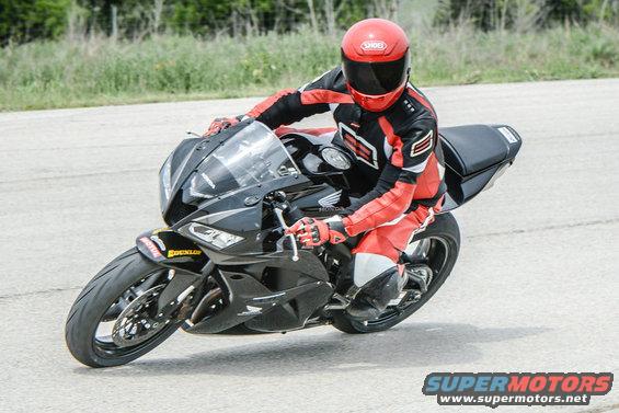 Black motorcycle with a rider in red and black gear, leaning into a turn