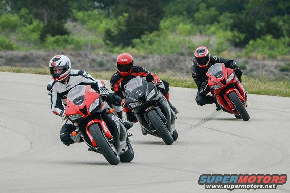 Three sport motorcycles with riders in full gear on a paved track, one red, one black, and another red