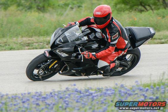 Motorcyclist in red and black leathers on a black sportbike, leaning into a turn
