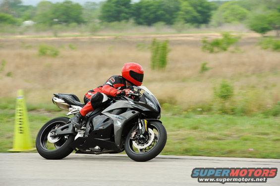 Rider in red gear on a black sportbike on a track with a yellow cone
