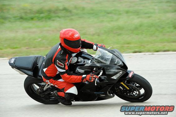 Motorcyclist in red and black leathers on a black sportbike, leaning into a turn. DUNLOP tire visible