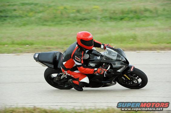 Black sport motorcycle with a rider in red and black gear leaning into a turn