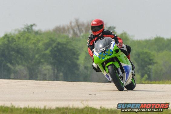 Rider in red and black gear on a green and white sportbike leans into a turn on a paved track