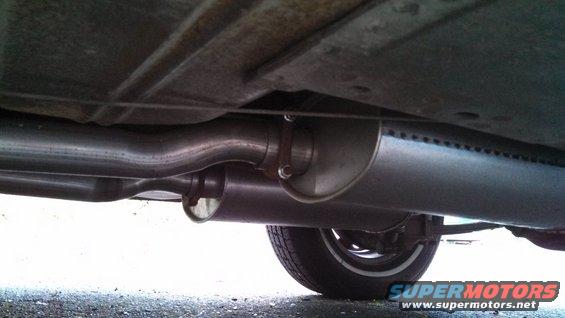 Underside of a car showing dual exhaust pipes, mufflers, and a tire with a white stripe