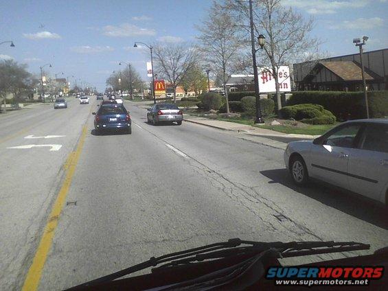 Silver sedan driving on a suburban street with other cars and businesses