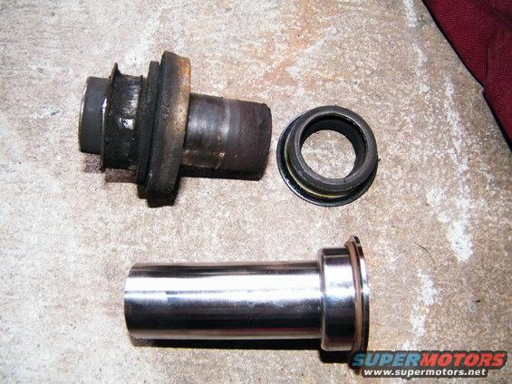 Disassembled suspension parts, including a metal sleeve and a rubber-lined metal piece, lie on a concrete surface