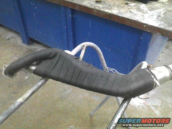 Exhaust pipe section wrapped in black heat tape, supported by metal stands