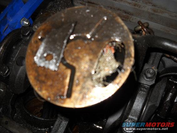 close-up of a damaged, greasy circular engine component with a hole torn in it