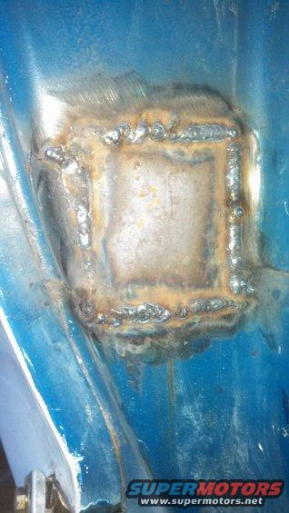Close-up of a square metal patch with visible weld marks on a blue surface