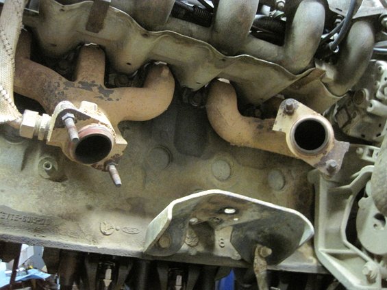 Engine block with exhaust manifolds attached. Some text and a Ford logo are visible on the block