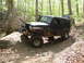 1979 Ford Bronco - A muddy Jeep Wrangler navigates a rocky, wooded trail, with another vehicle following behind.