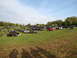 1979 Ford Bronco - A large gathering of off-road vehicles are parked in a grassy field under a partly cloudy sky.