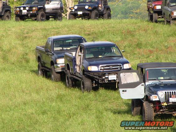 Several off-road vehicles parked on a grassy slope, including a blue Toyota Tundra and a Jeep Wrangler