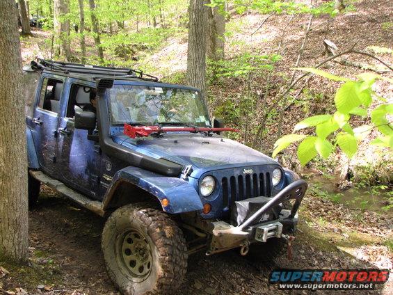 Blue Jeep Wrangler with snorkel and roof rack on a wooded trail